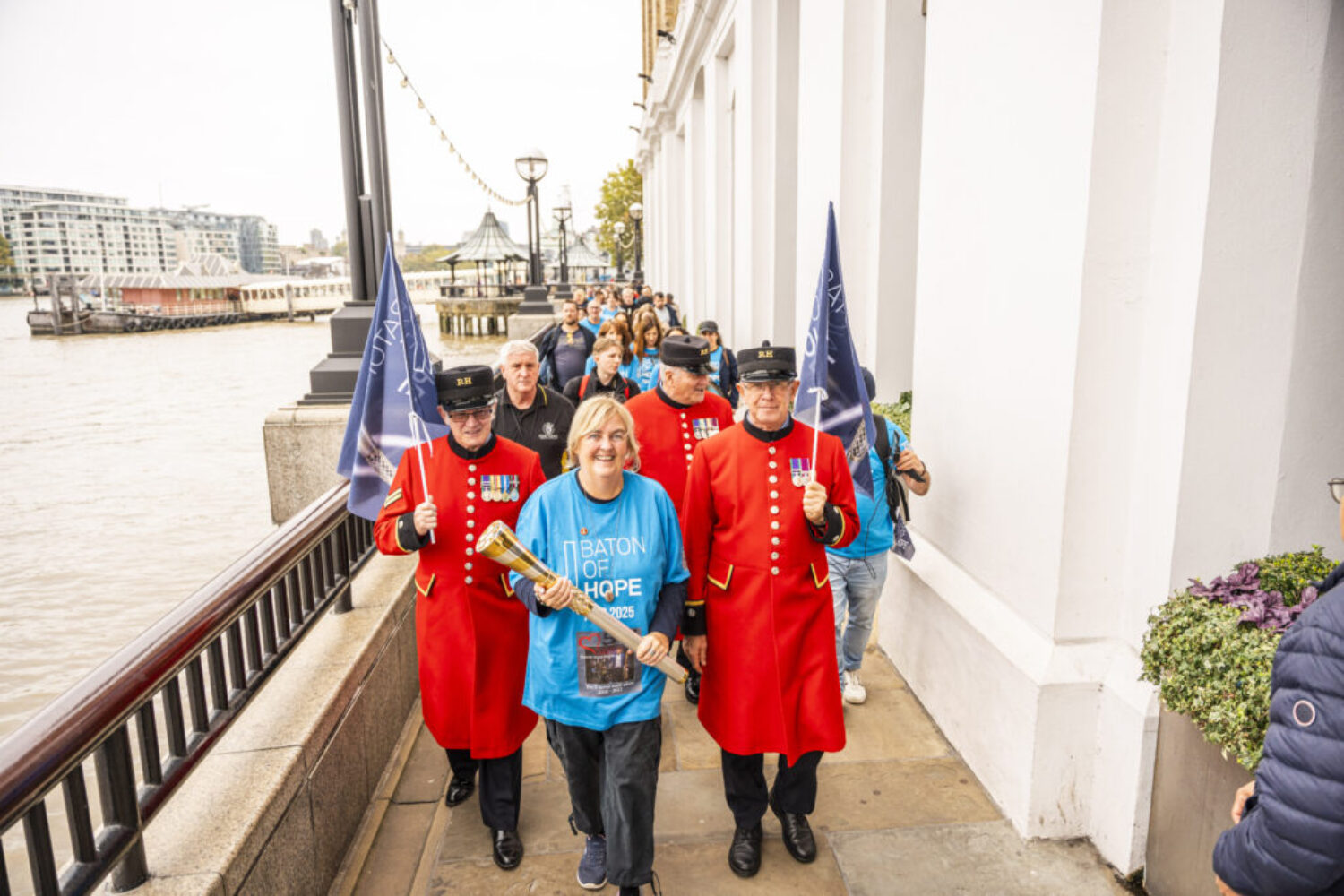 A photo of a woman carrying a decorative metal baton, with people with flags walking behind her in London.