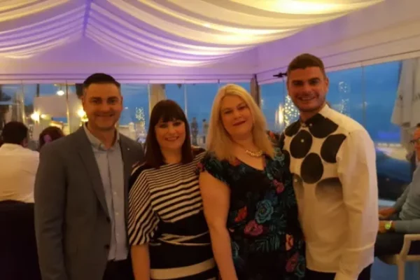 A photo of a group of people inside a wedding marquee venue in the evening hugging and smiling for the camera.