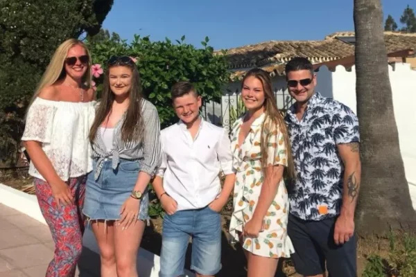 A family in a photo together on holiday outside in front of a hedge wearing holiday clothes.