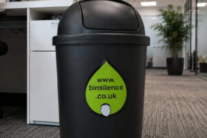 A black waste paper bin placed in an office.