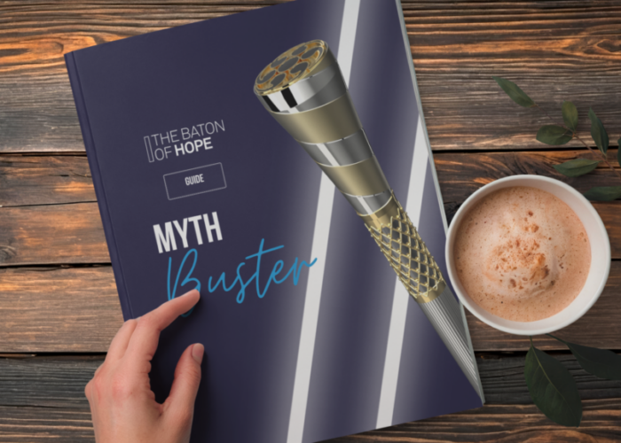 A mockup design of a Myth Buster printed guide on a wooden table next to a cup of coffee with a hand holding the guide.