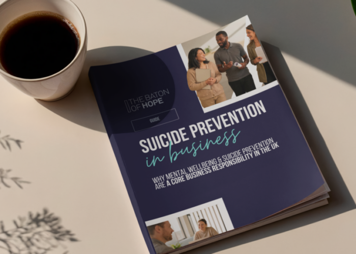A mock up of a Suicide Prevention in Business printed guide placed on a light neutral surface next to a coffee cup.