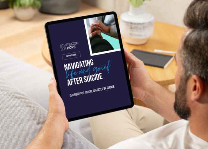 A mockedup design of a man sat on a sofa looking at a Suicide Support Guide on an iPad in his hands.