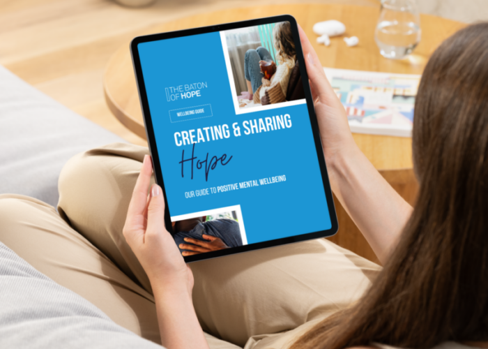 A mockedup design of a woman sat on a sofa looking at a Wellbeing Guide on an iPad in her hands.