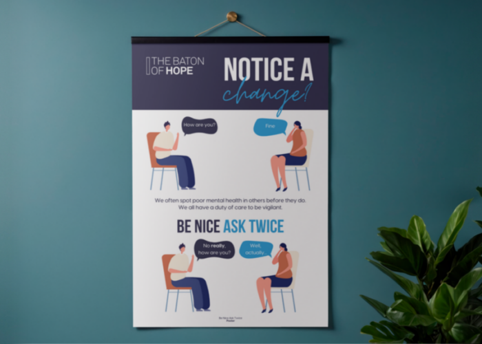 A mockup design of a poster on a dark blue wall with a house plant to one side of it.